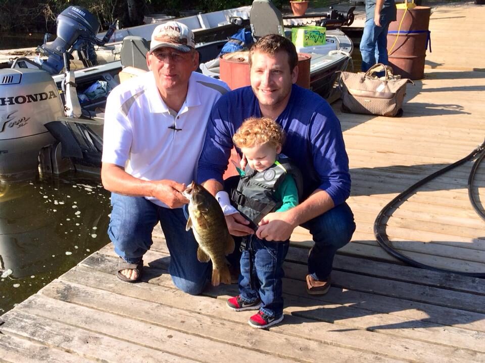 Grandfather, father and young grandson on the dock holding a bass